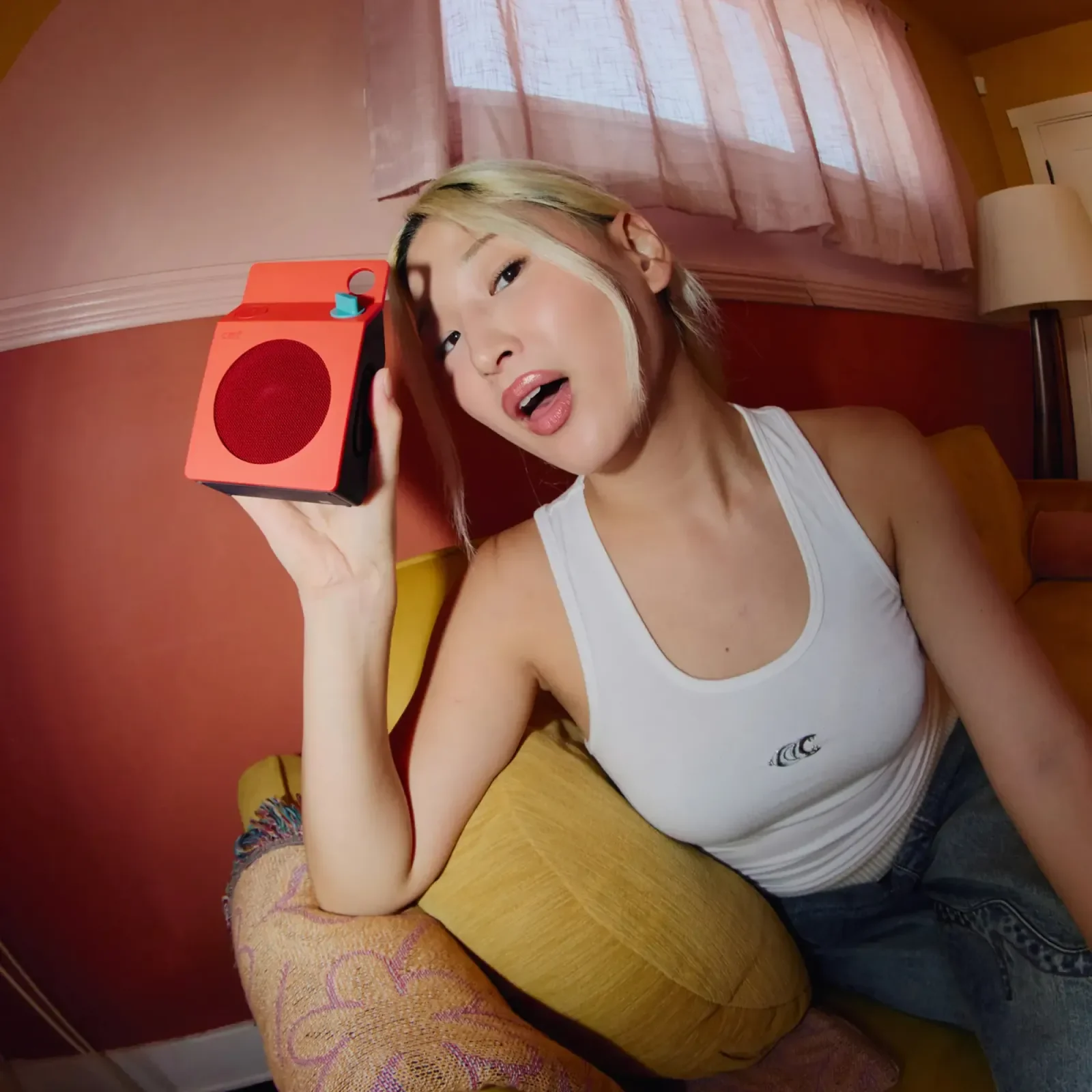 Wanita memegang CMF Speaker S warna oren dekat telinga sambil duduk di sofa