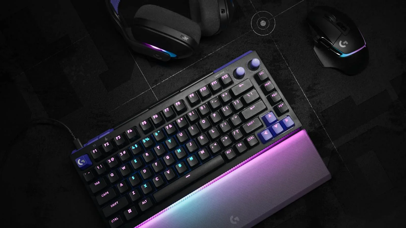 Keyboard, tetikus dan headset Logitech G di atas meja gelap dengan lampu RGB ungu