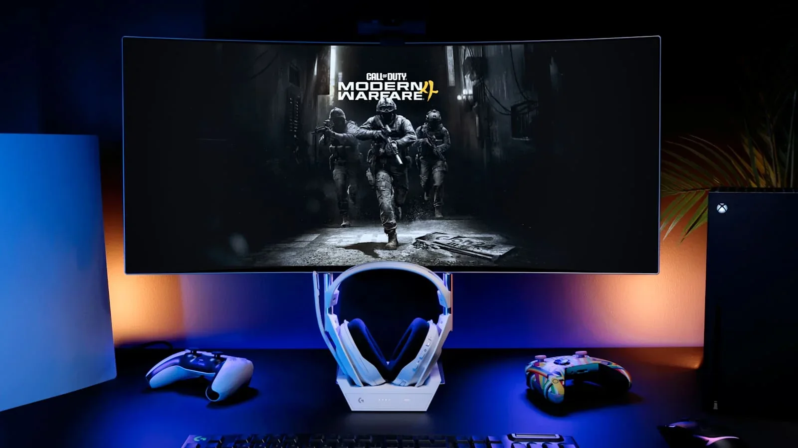 Setup gaming dengan monitor melengkung memaparkan Call of Duty Modern Warfare 4, headset Astro putih dan dua controller