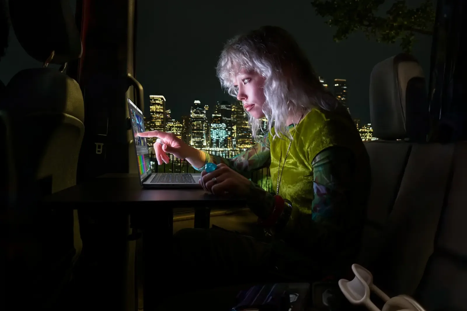 Gambar: Apple Pengguna guna MacBook Pro PROLED XDR dalam gelap dengan pemandangan bandar bercahaya di belakang