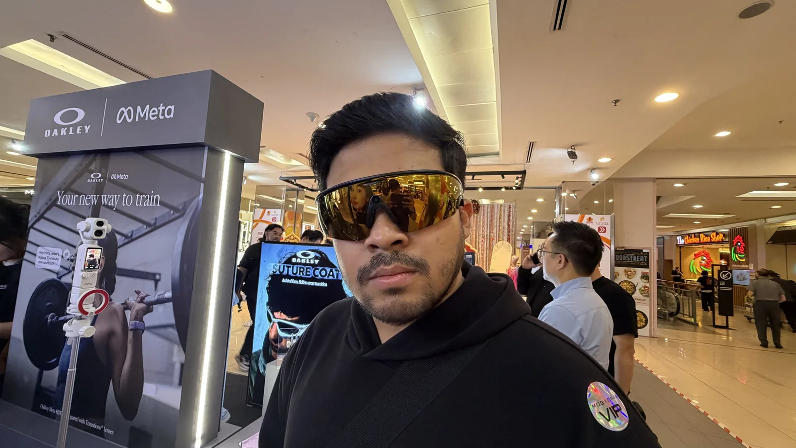 Lelaki memakai Oakley Meta Vanguard kanta emas di depan booth Oakley Meta dengan tulisan Your new way to train